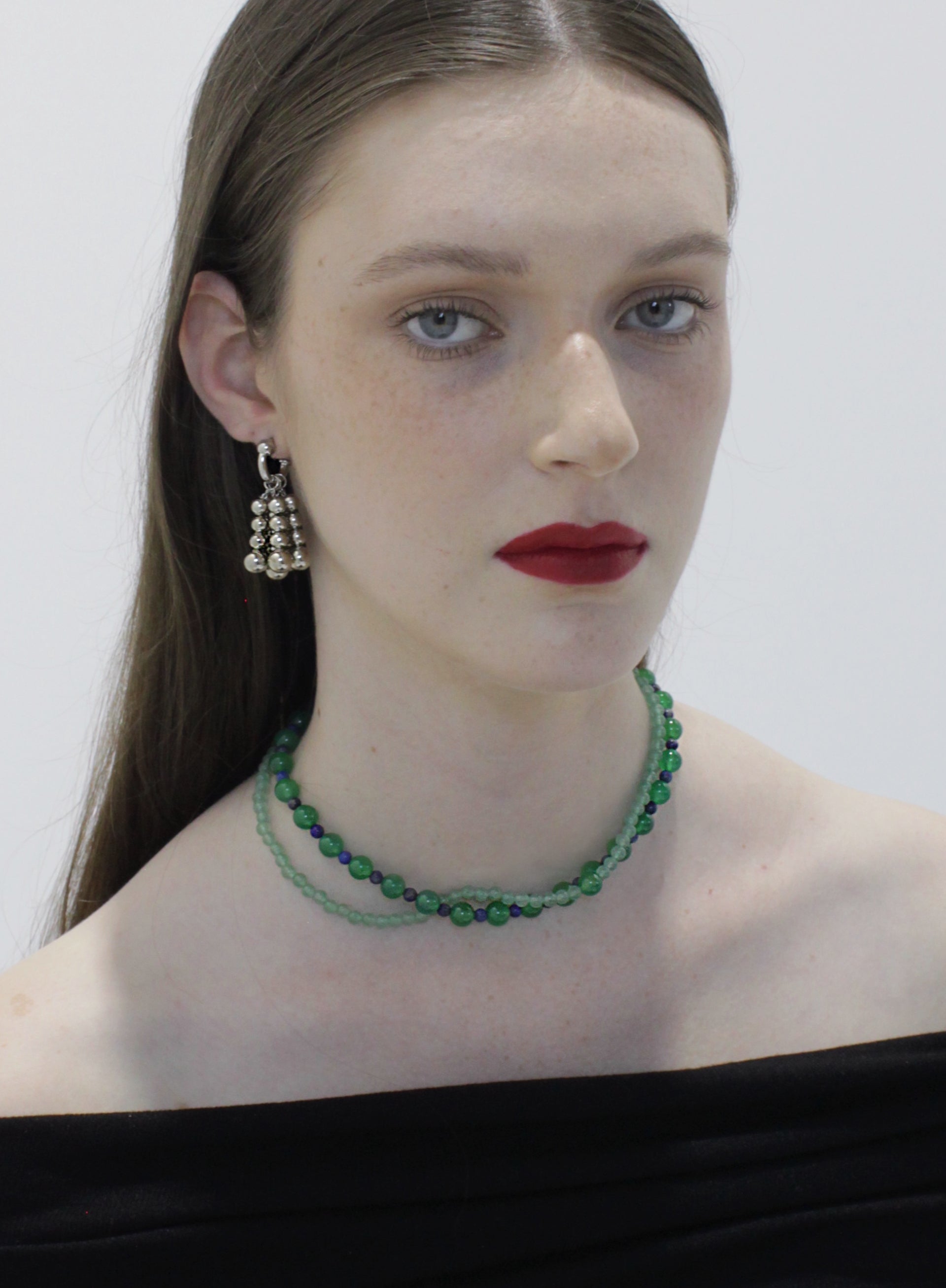 Woman wearing a green beaded necklace and silver earrings against a white background