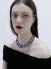 Woman wearing a purple beaded necklace against a white background