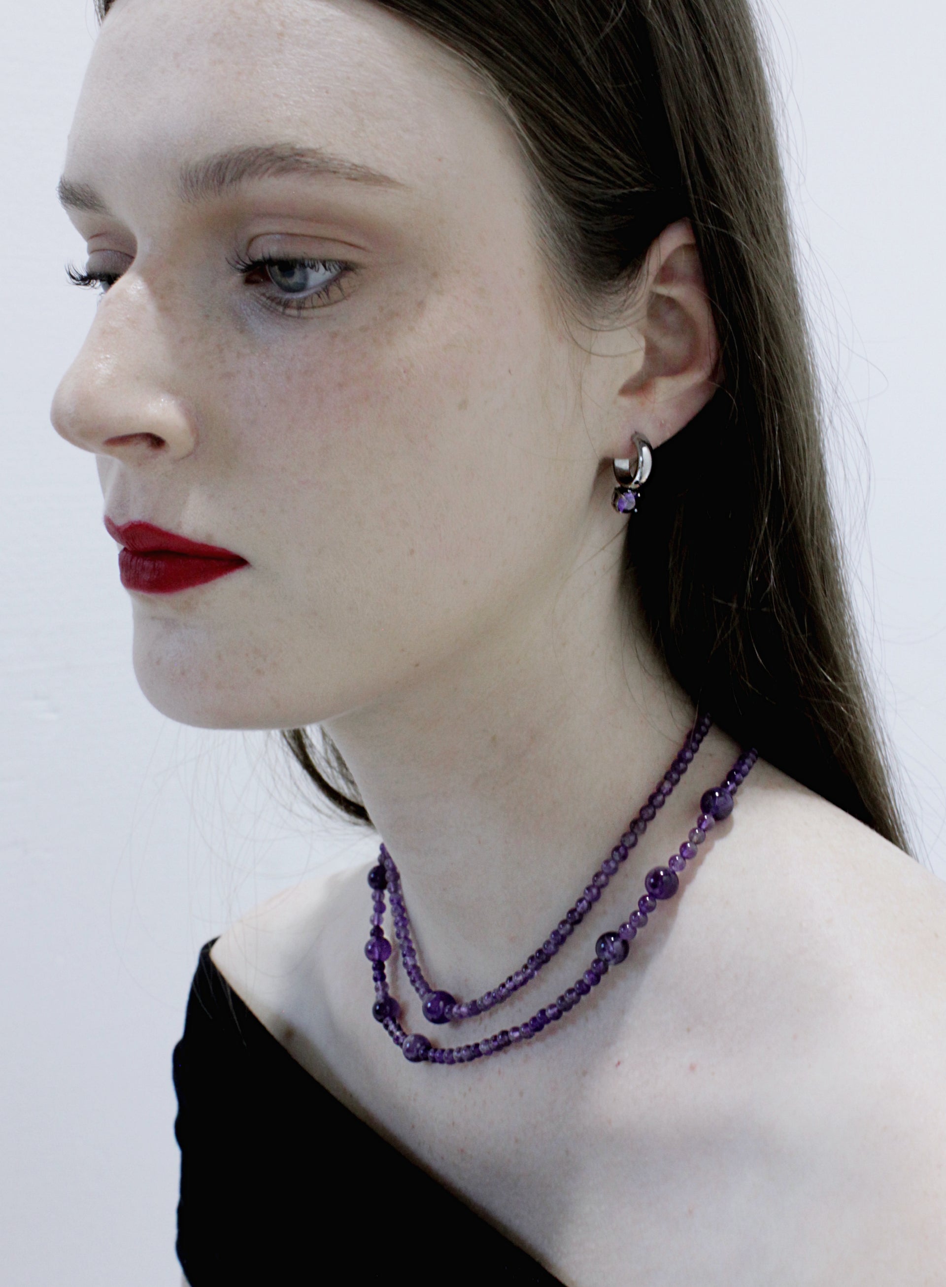 Woman wearing a purple beaded necklace and earrings against a white background