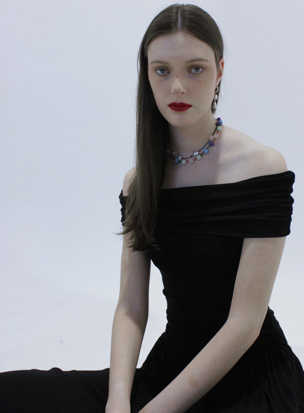 Woman wearing a black off-shoulder dress with silver earrings and colourful beaded necklace on a white background