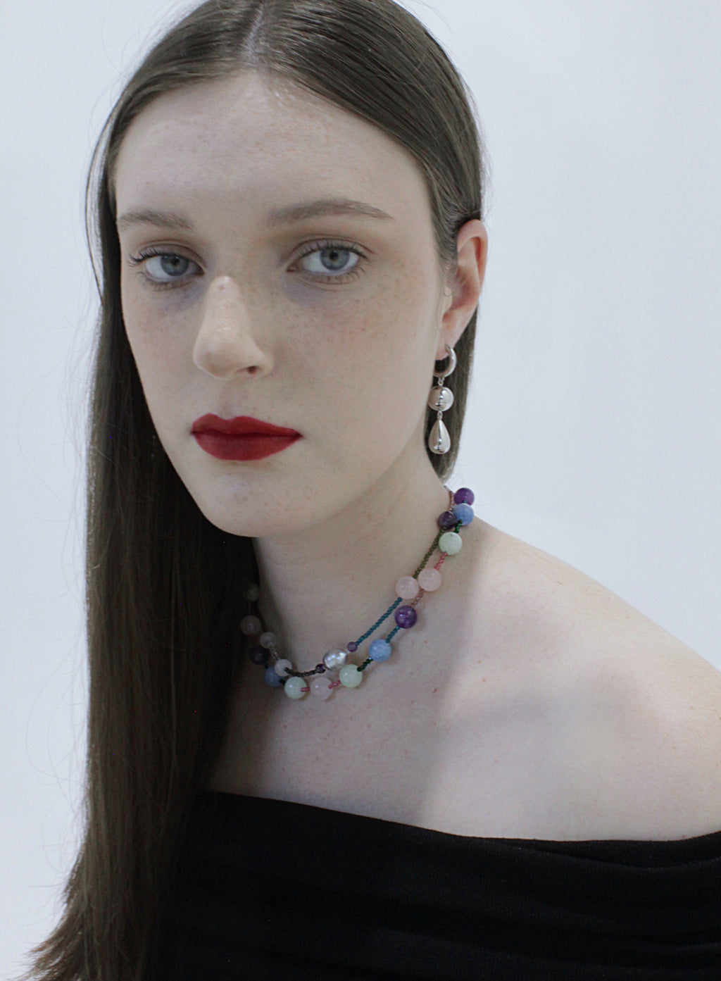 Woman wearing a colorful beaded necklace and silver drop earrings against a white background