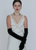 Woman wearing a white lace dress with black gloves on a plain background