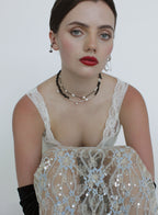Woman wearing a white lace top with sequin detailing on a plain background