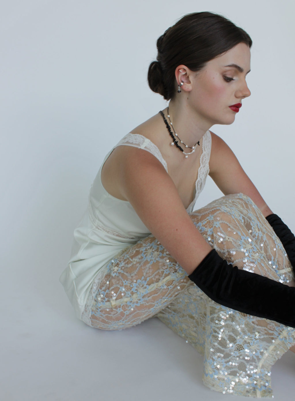 Woman in a white top and sequin skirt sitting on a white background