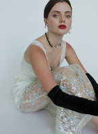 Woman wearing a white lace top and black gloves sitting on a white background