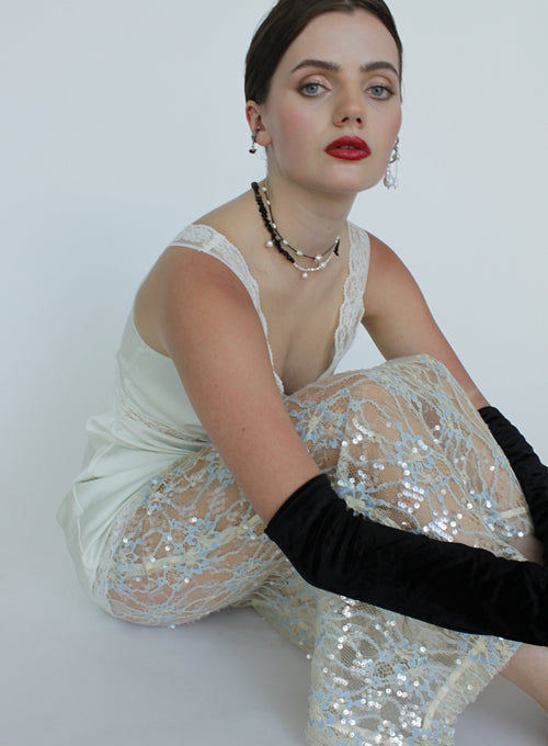 Woman wearing a white lace top and black gloves sitting on a white background