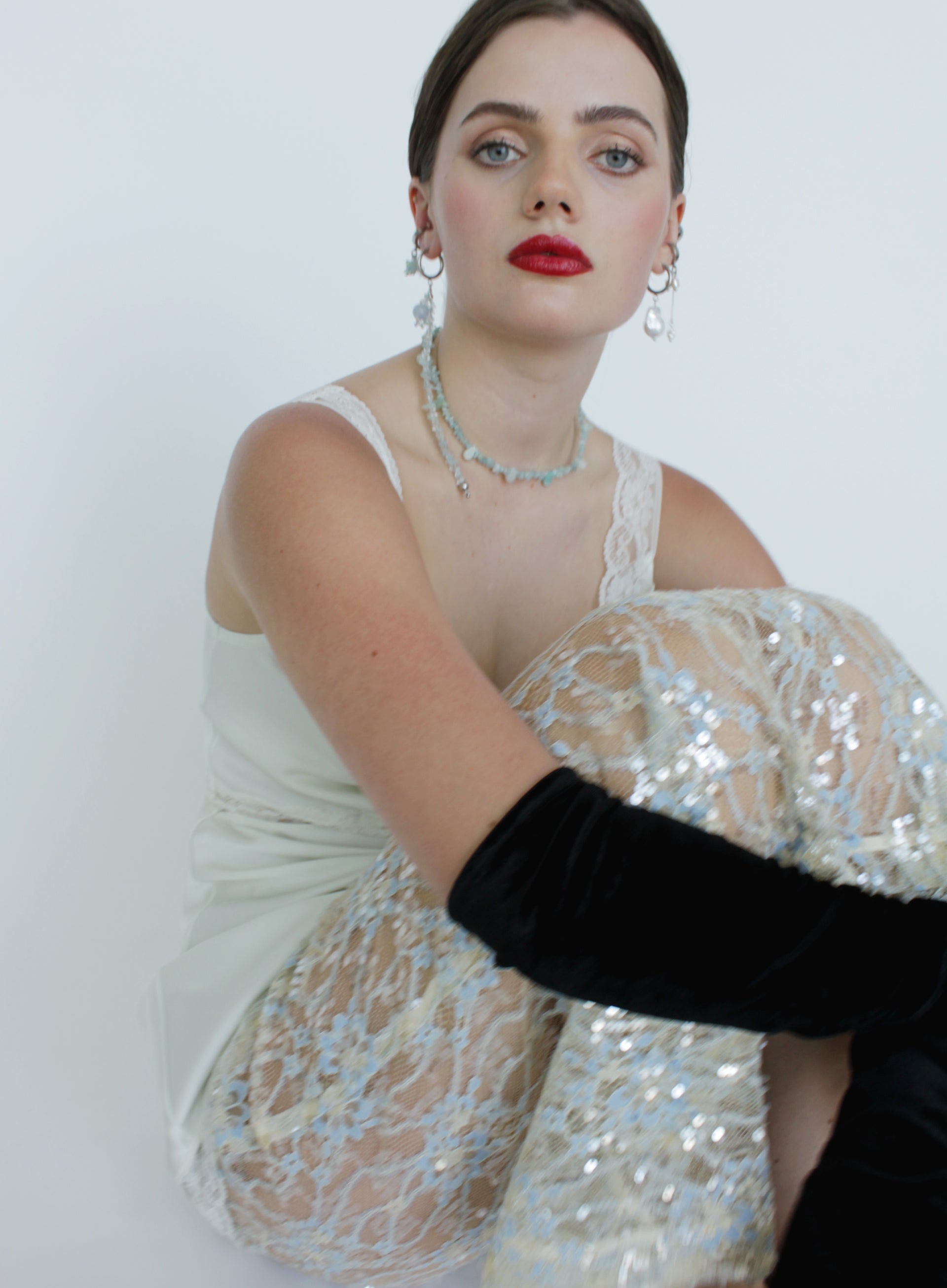 Woman wearing a white lace top and black gloves with a sequined silver skirt against a white background