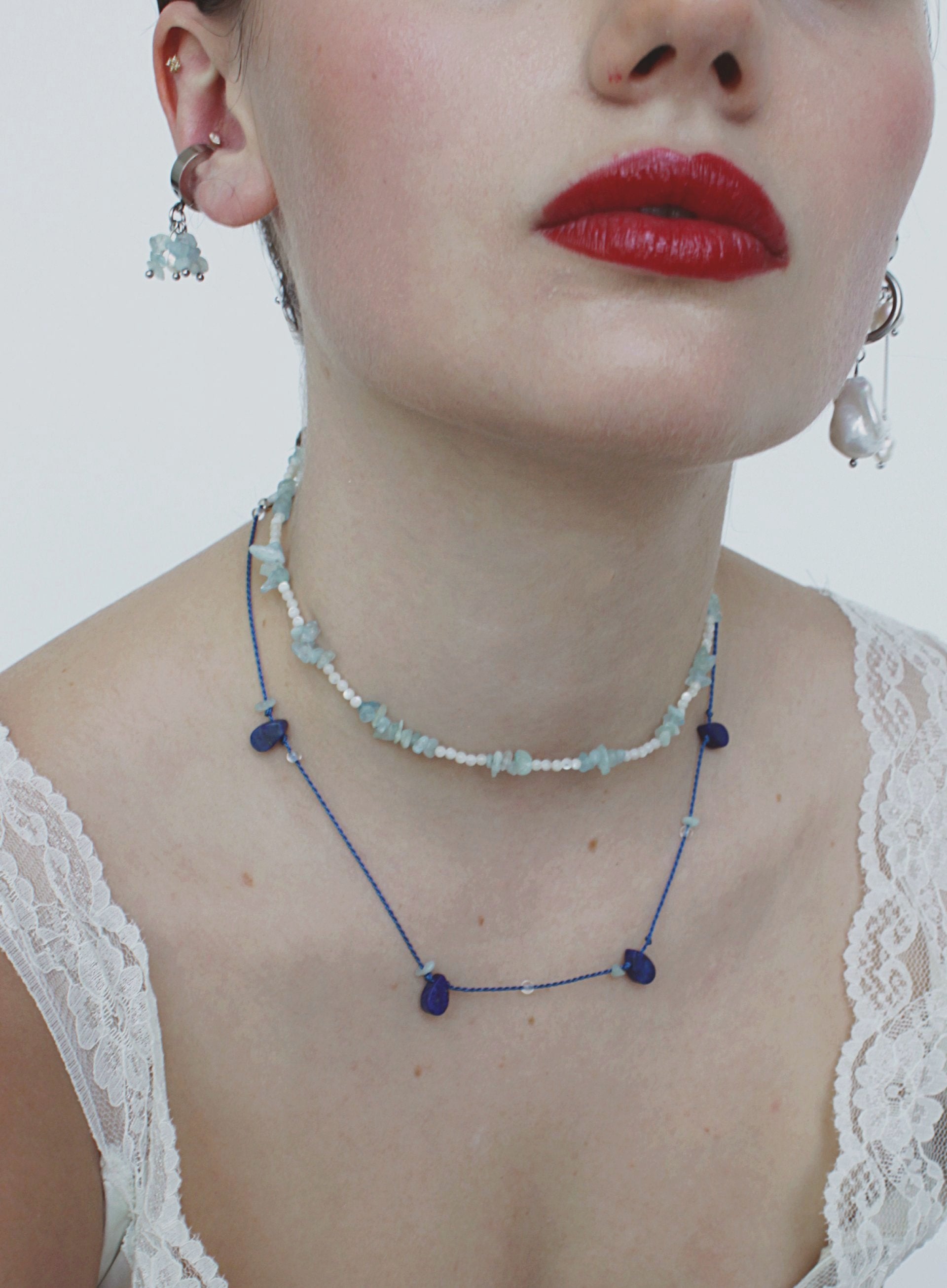 Close-up of a person wearing a beaded necklace and earcuff with a plain background