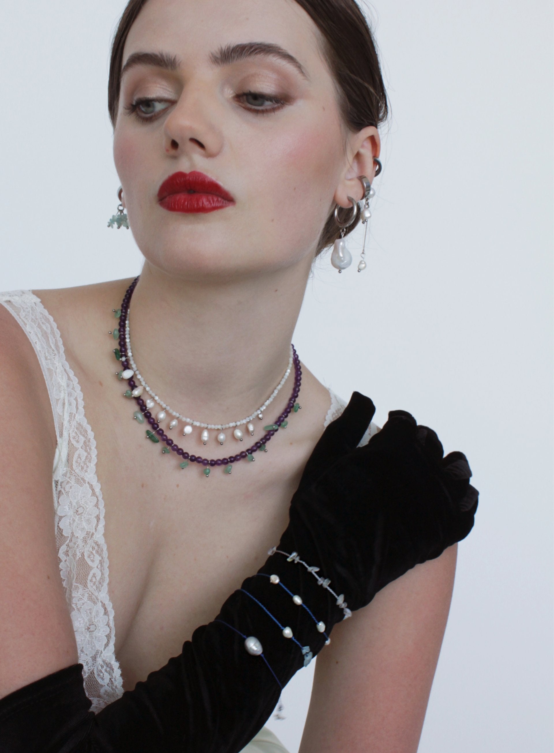 Woman wearing a double layered necklace, earrings, and a black glove with a white background