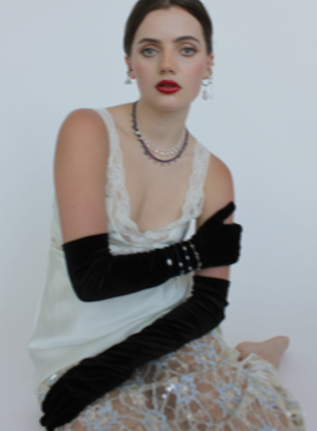 Woman wearing a white dress with black gloves and red lipstick against a plain background