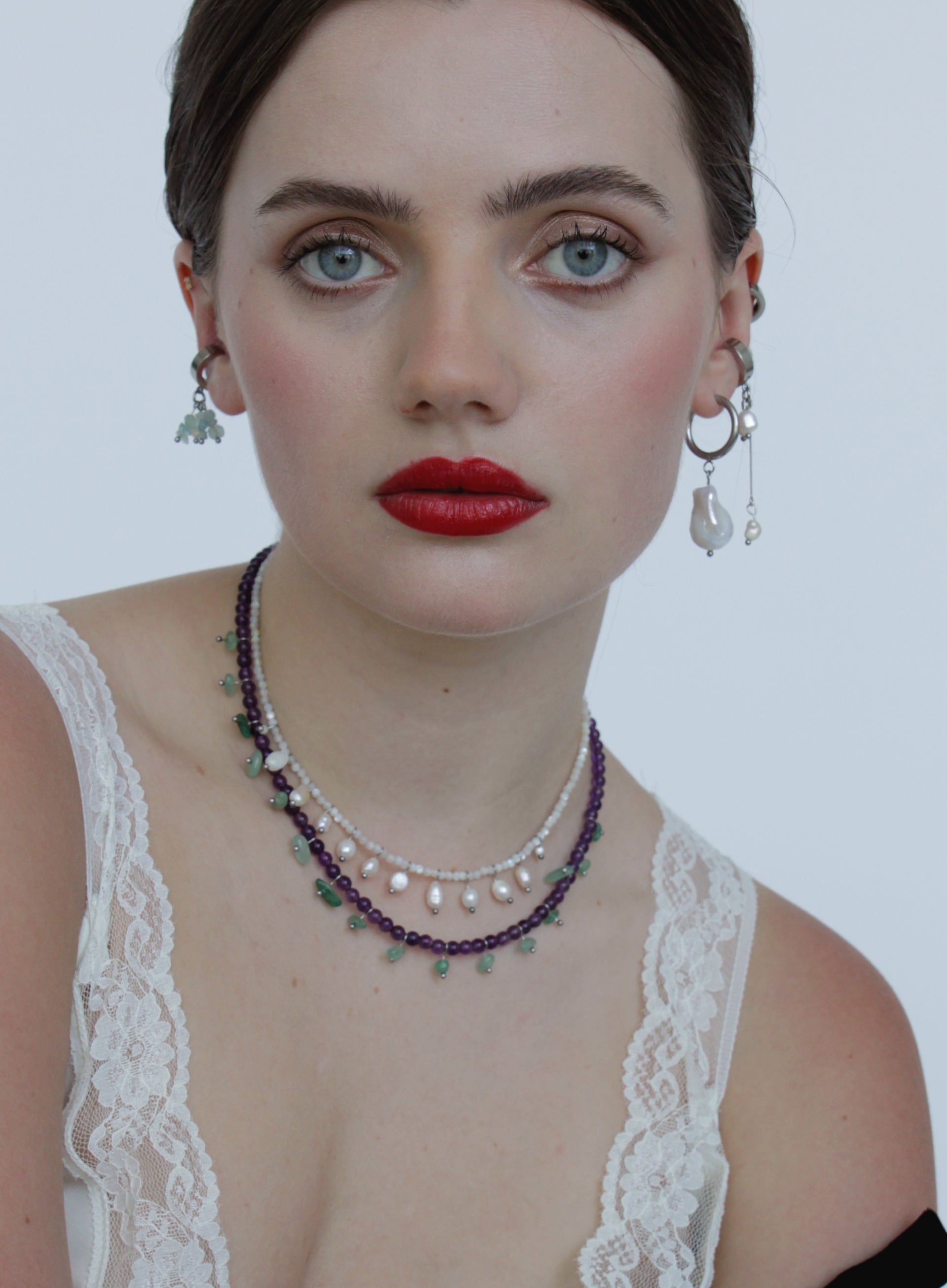 Woman wearing a necklace and earrings with a white lace top against a plain background