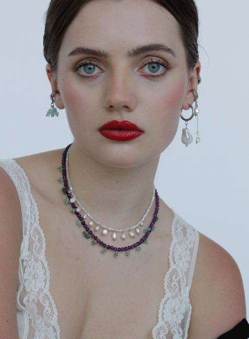 Woman wearing a necklace and earrings with a white lace top against a plain background