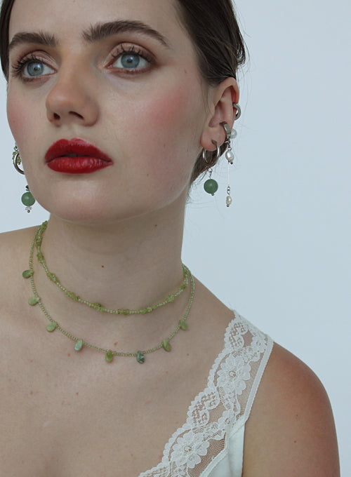 Woman wearing a green beaded necklace and earrings against a plain background