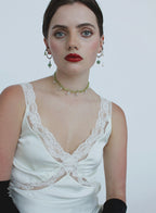 Woman wearing a white lace top with and green necklace on a plain background
