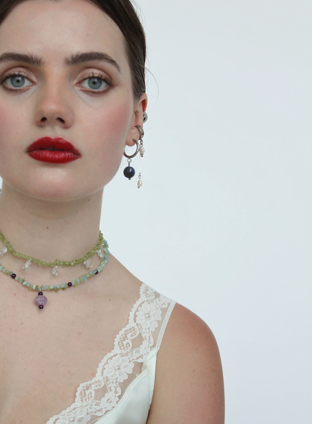 Woman wearing a necklace and earrings with a white lace top on a plain background