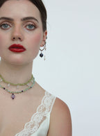 Woman wearing a necklace and earrings with a white lace top on a plain background