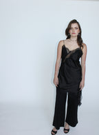 A woman modeling a black satin camisole top with lace trim and matching wide-leg pants against a plain white studio background.