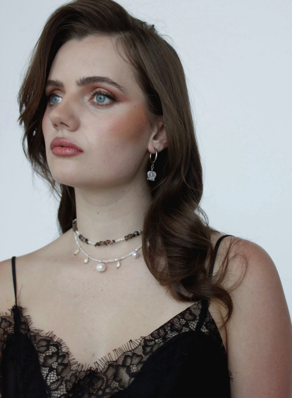 Woman wearing a black lace top and layered necklaces against a plain background