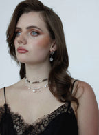 Woman wearing a black lace top and layered necklaces against a plain background