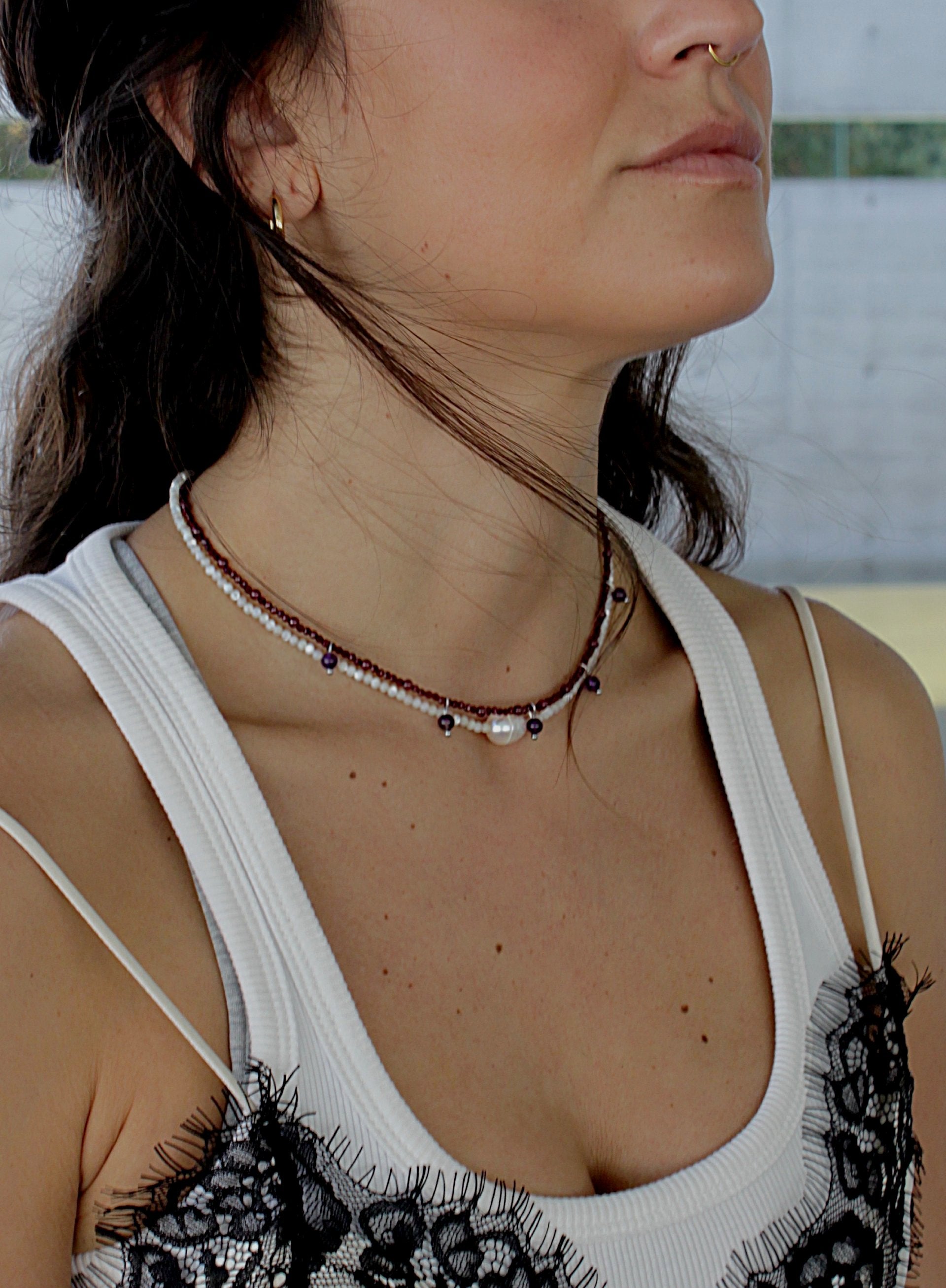 Close-up of a woman wearing a beaded pearl and garnet necklaces with a blurred background