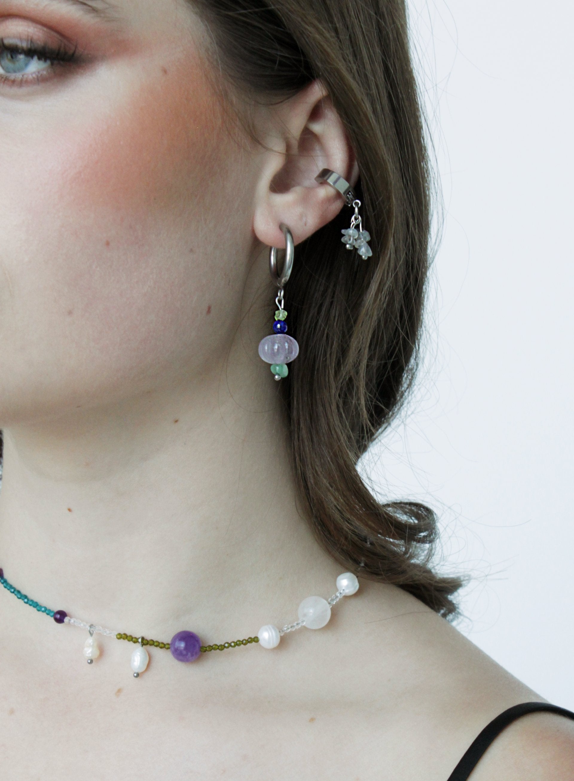 Close-up of a person wearing colorful beaded earrings and a necklace with a plain background