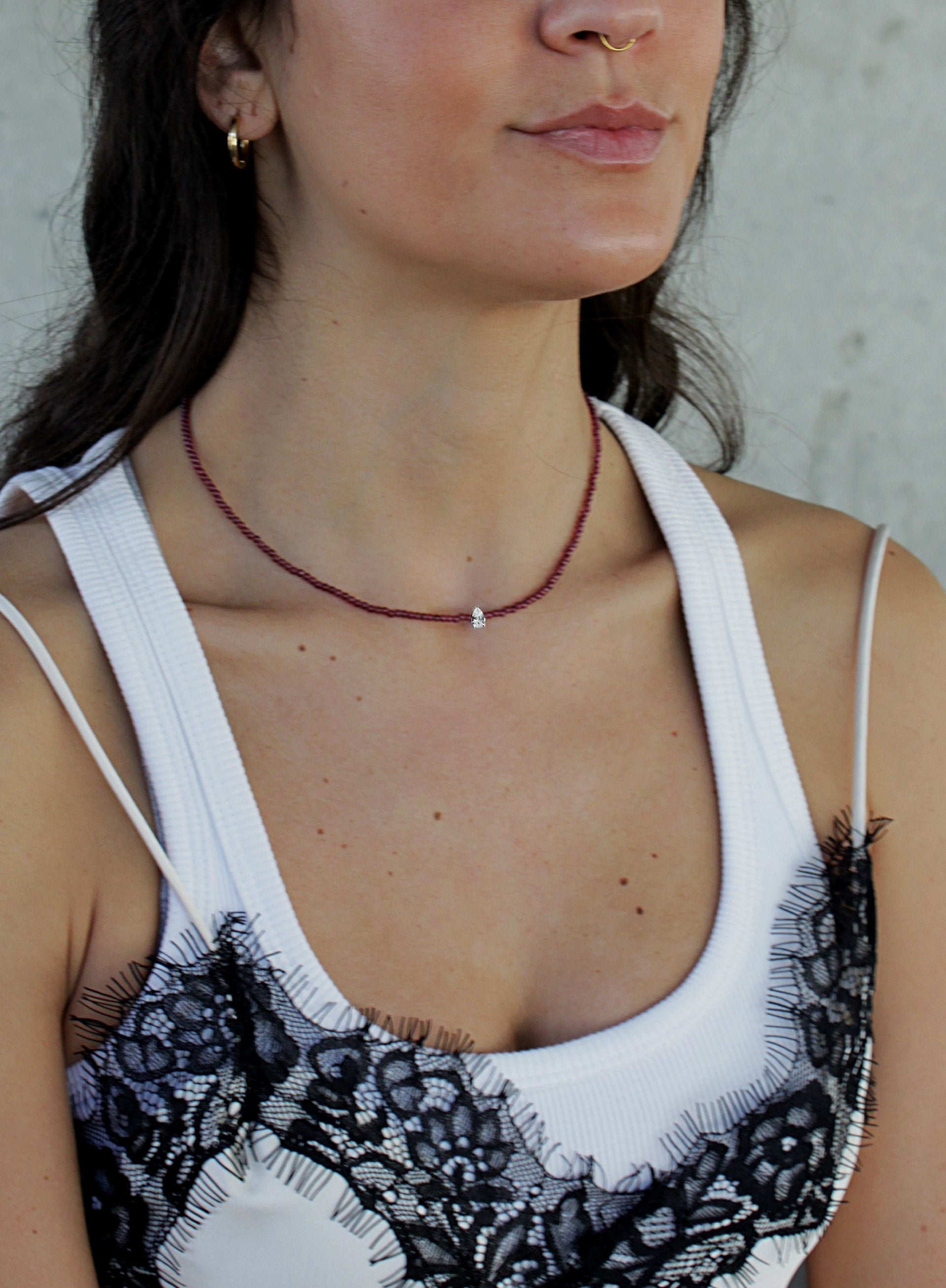 Woman wearing a white top with black lace details and a red garnet necklace.