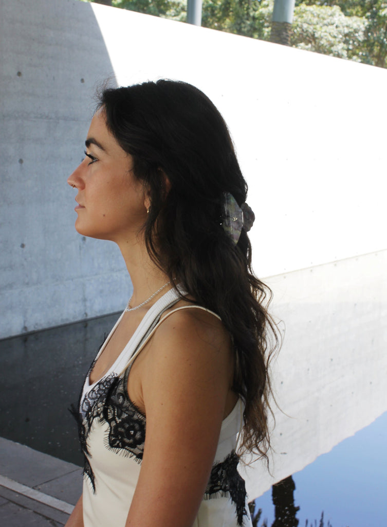 Woman with long dark hair standing against a light-colored wall with hair claw