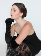 Woman wearing a black dress with floral details and a black glove, against a white background