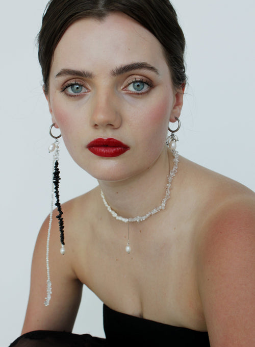 Woman wearing a black dress with red lipstick and pearl jewelry against a white background