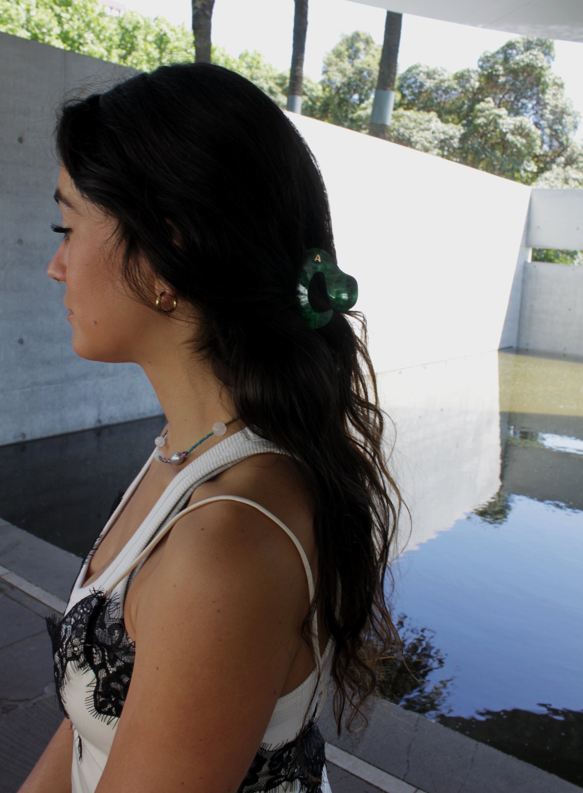 Woman with a green hair claw standing outdoors near a pool.