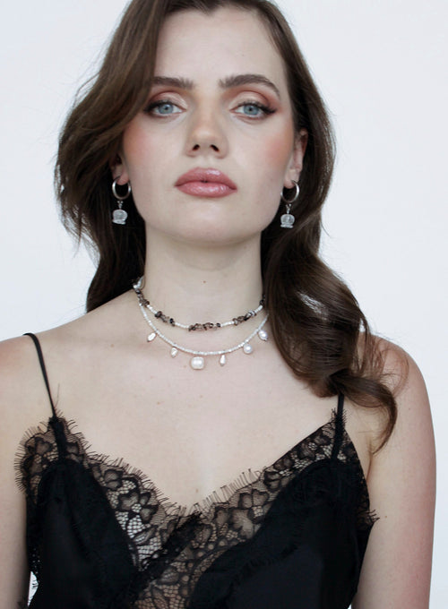 Woman wearing a black lace top and multiple necklaces with a white background