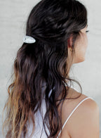 Woman with wavy hair tied back with a white barette against a light background