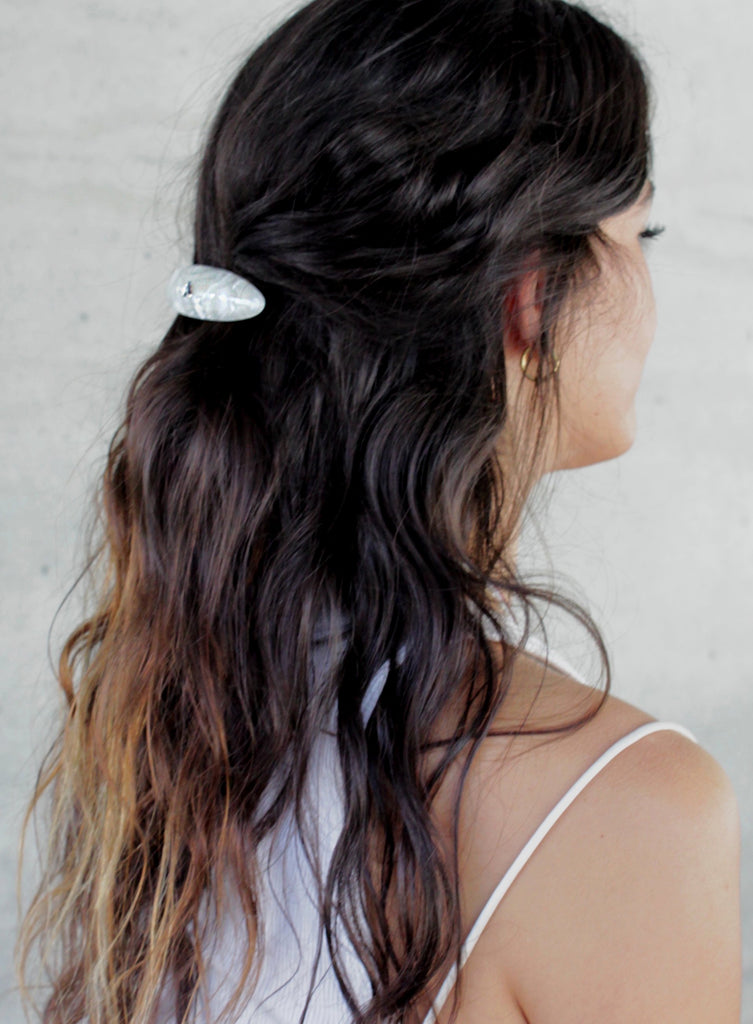 Woman with wavy hair tied back with a white barette against a light background