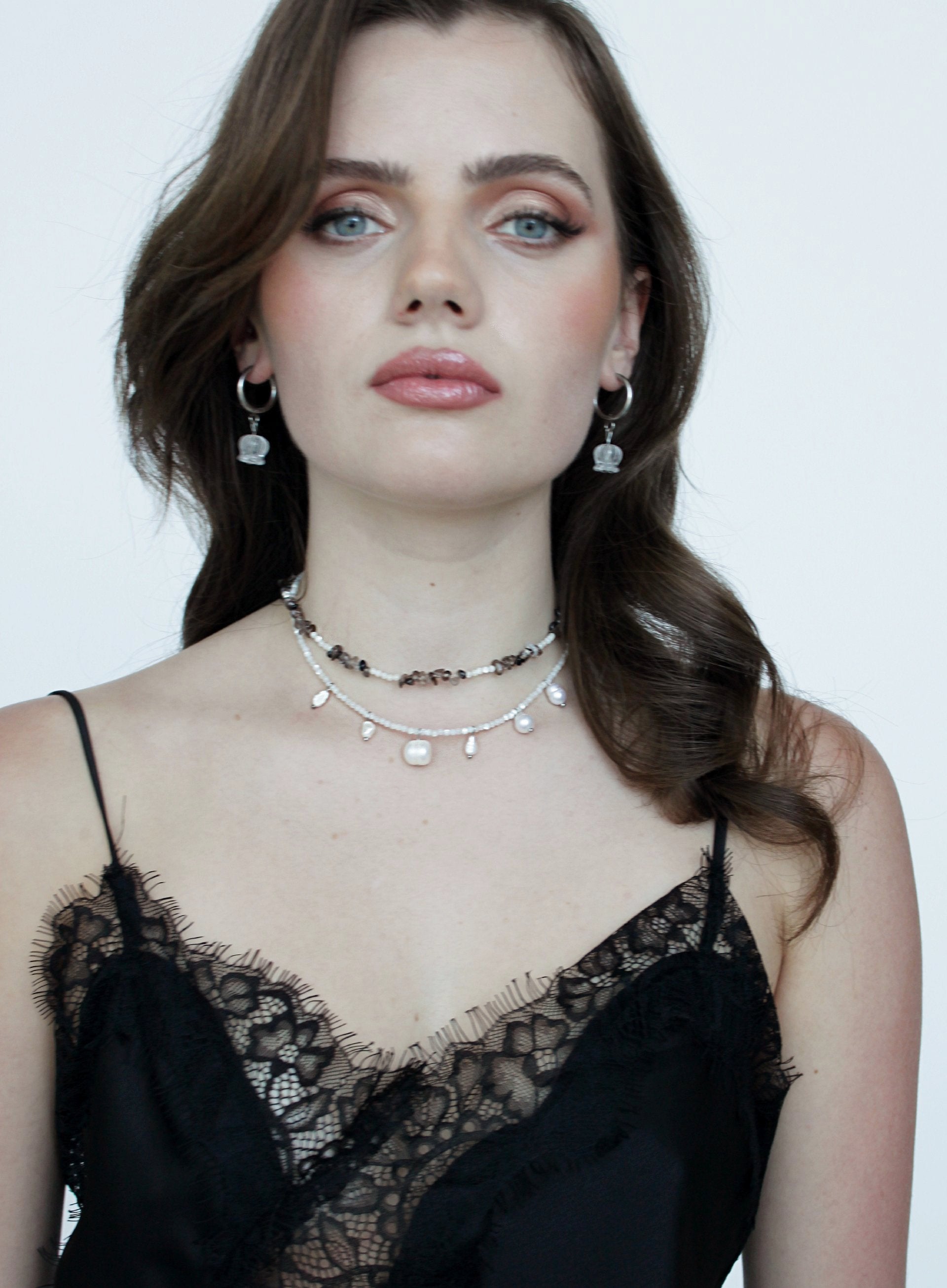 Woman wearing layered necklaces and earrings against a plain background