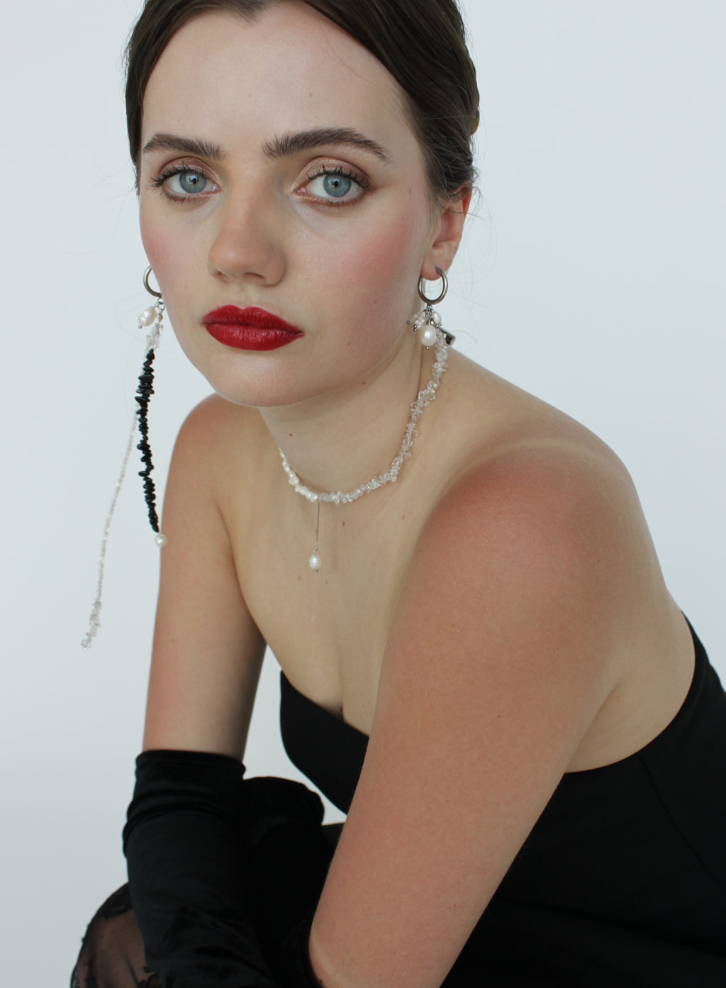 Woman wearing a black dress with red lipstick and jewelry against a white background