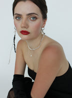 Woman wearing a black dress with red lipstick and jewelry against a white background