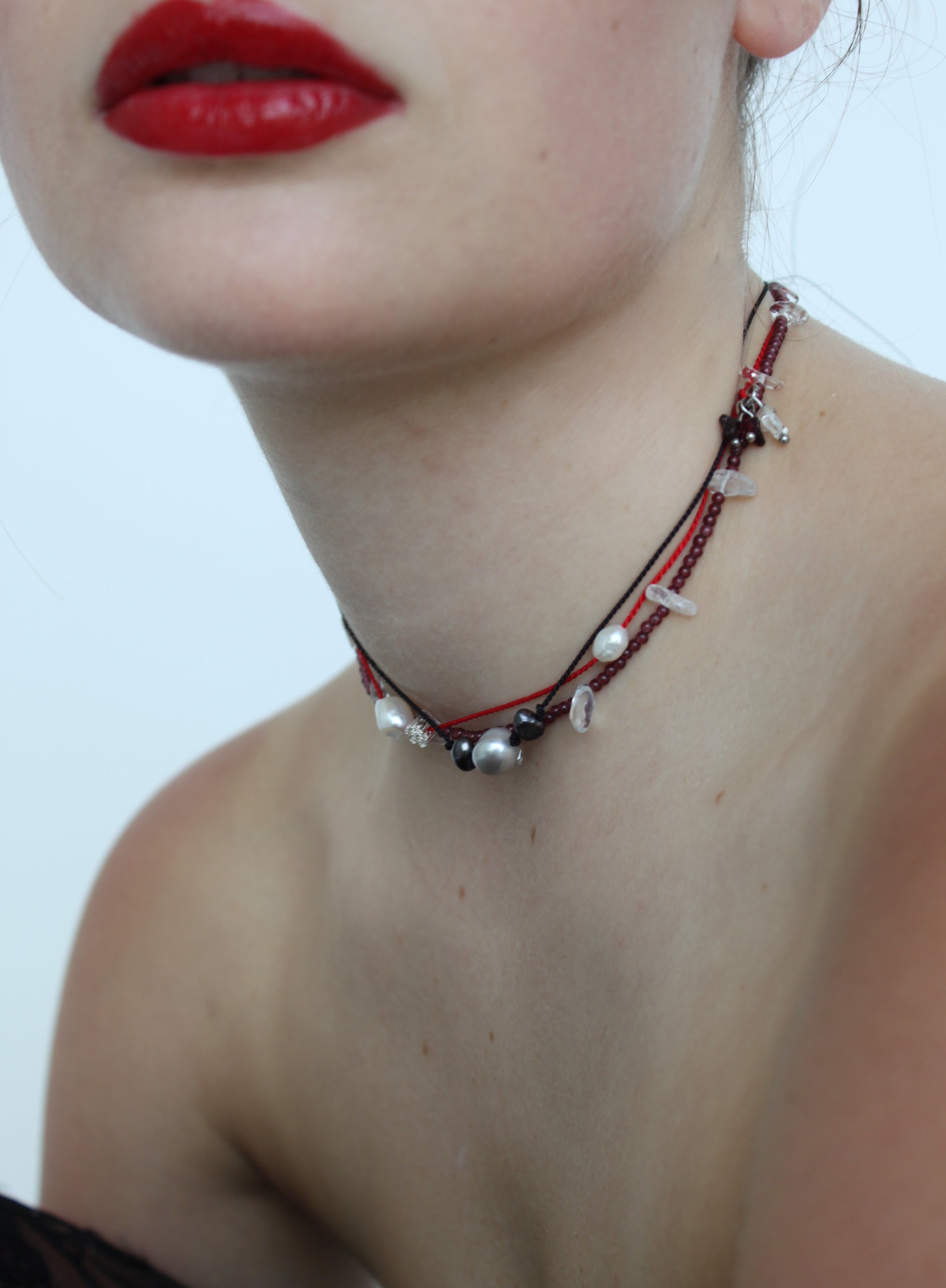 Close-up of a person wearing a delicate necklace with red, black, and silver elements.