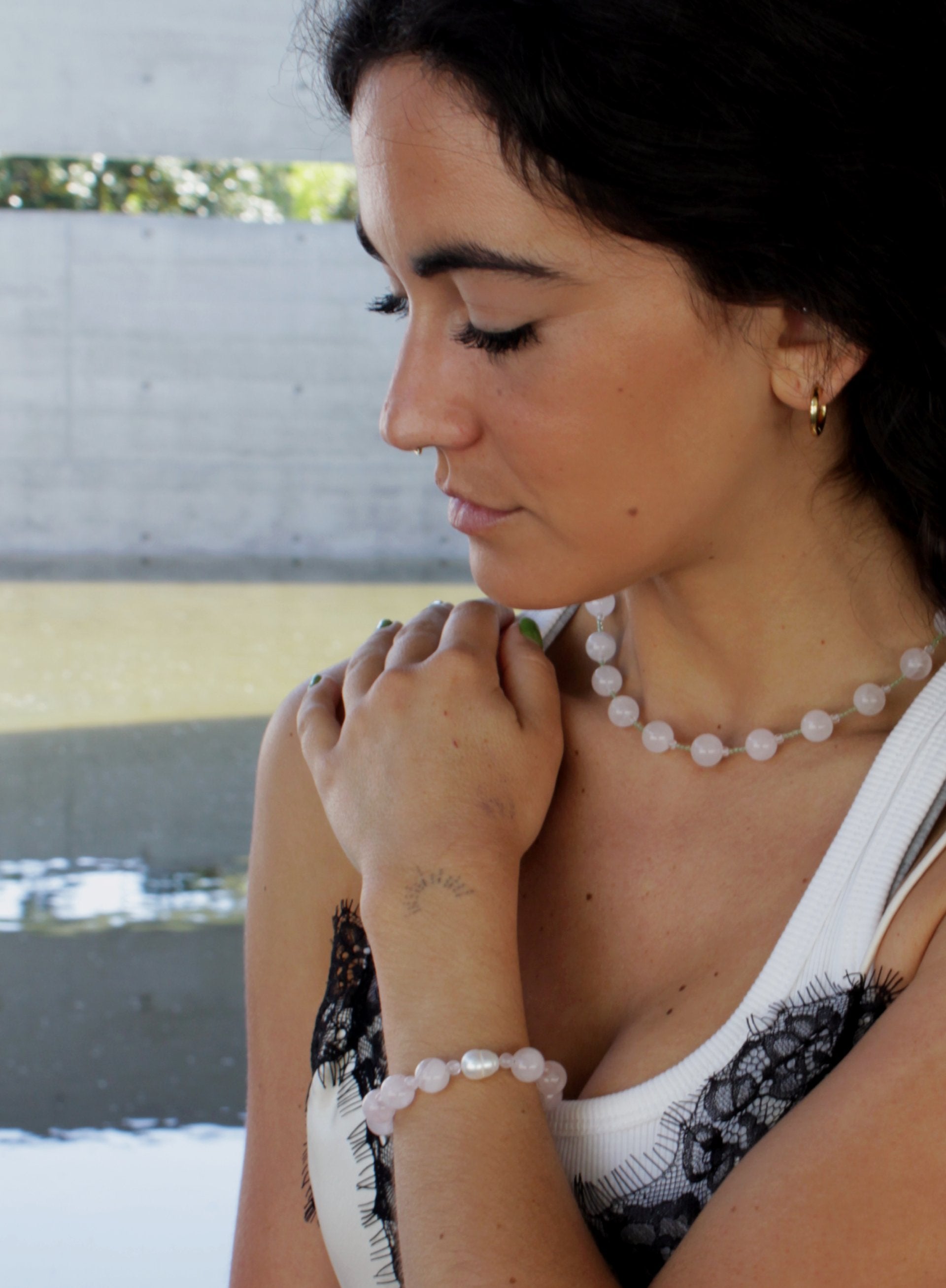 Woman wearing a rose quartz beaded necklace and pearl bracelet against a blurred background