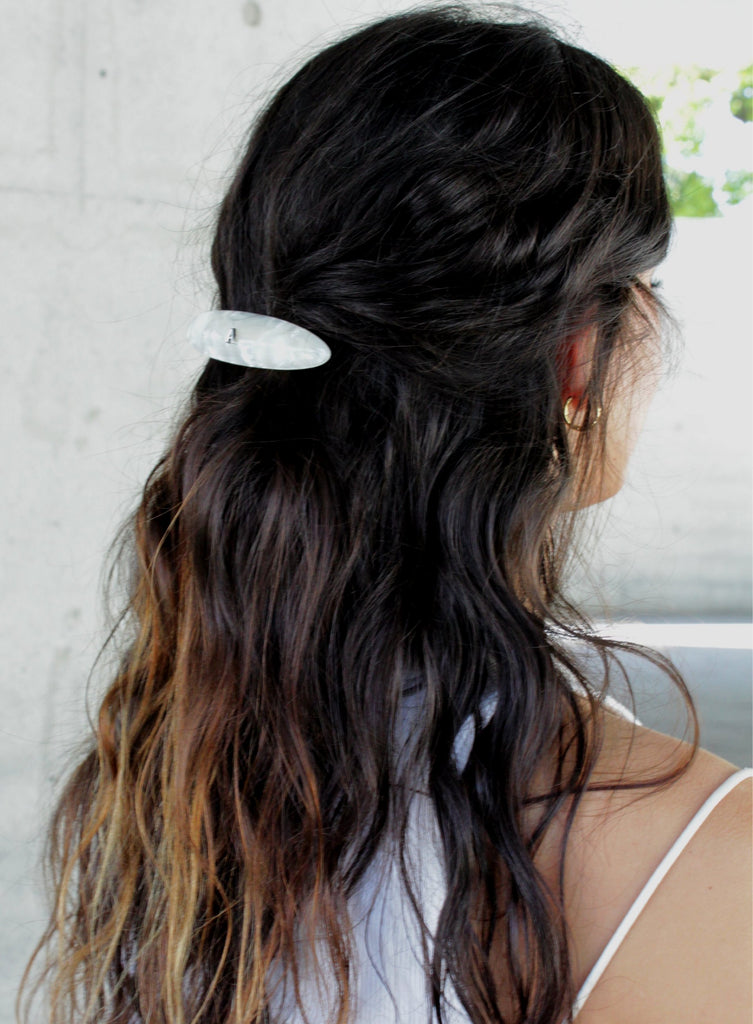 Woman with wavy hair tied back with a white barette against a light background