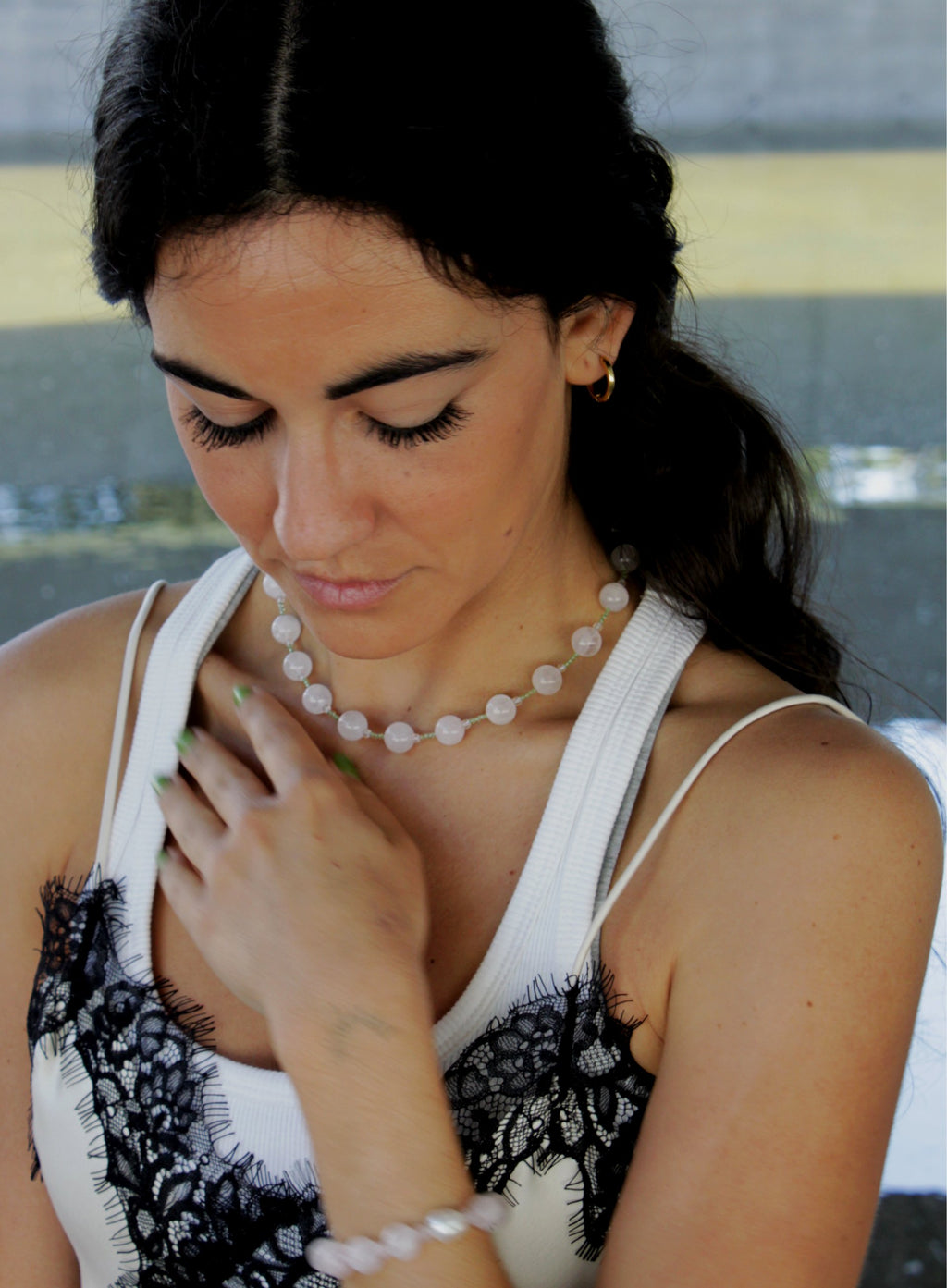 Woman wearing a rose quartz necklace and pearl bracelet with a blurred background