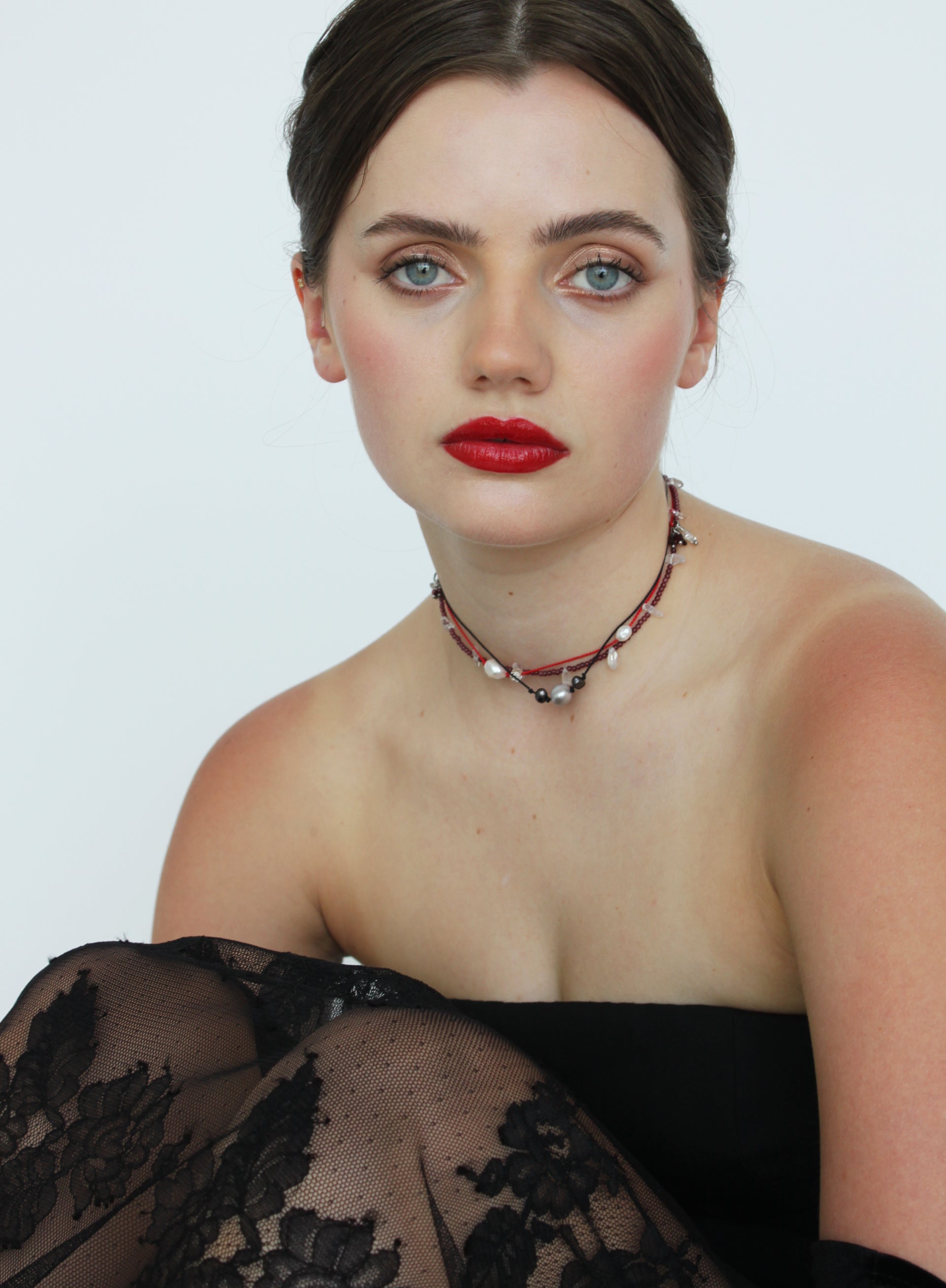 Woman wearing a black lace top with necklaces on a plain background