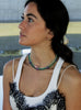 Woman wearing a white top with black lace details and a green beaded necklace.
