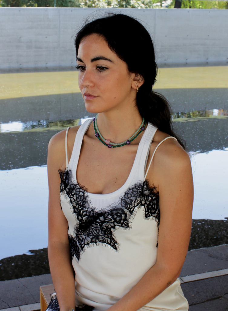 Woman wearing a white top with black lace details and a green beaded necklace.