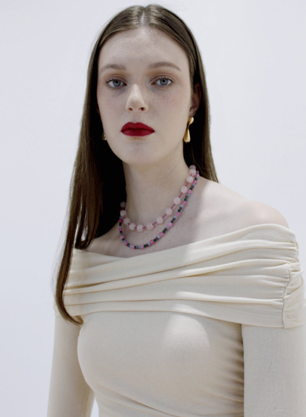 Woman wearing a white off-shoulder top and a colorful beaded necklace against a plain background