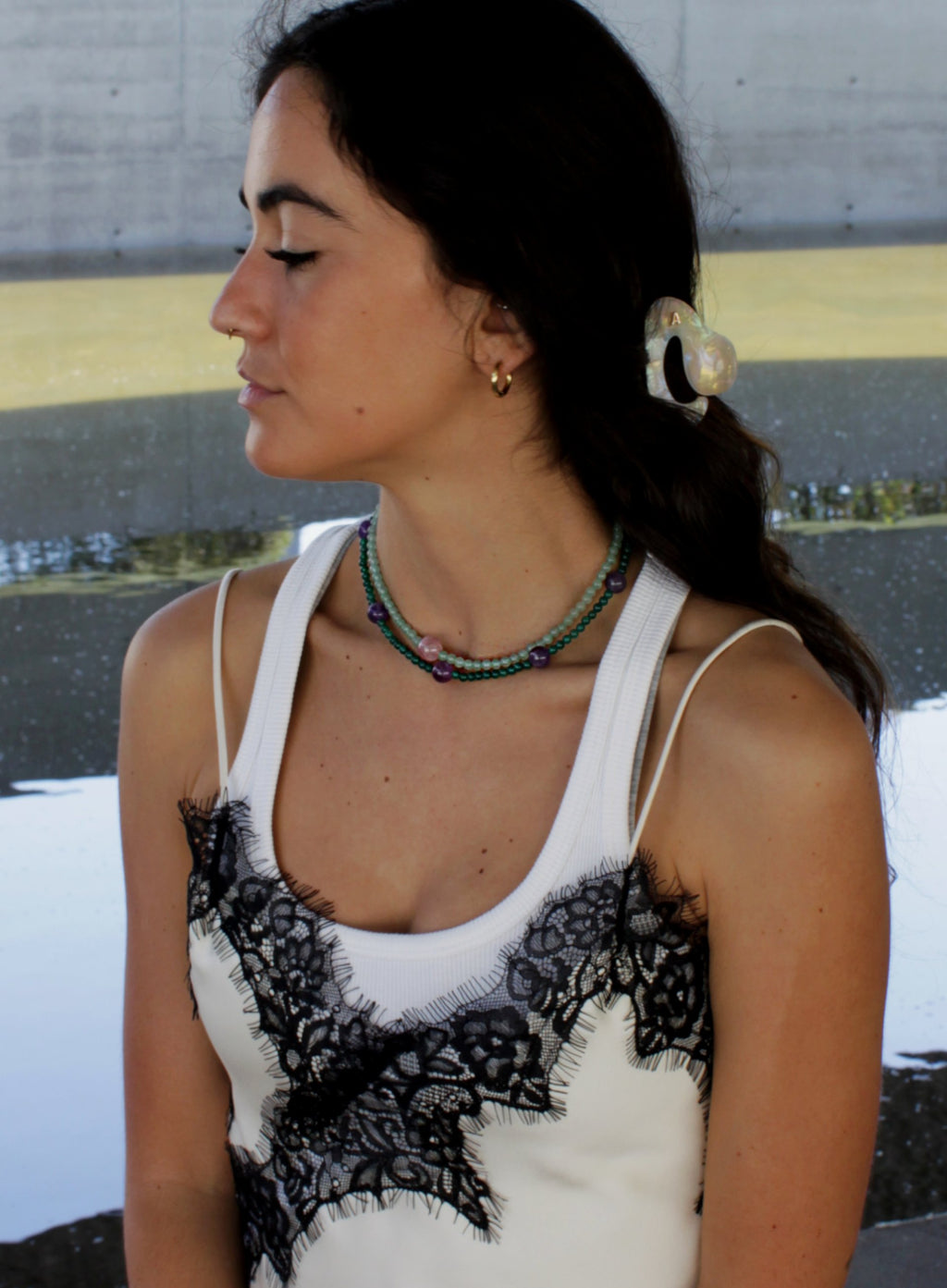 Woman wearing a white top with black lace details and a green beaded necklace.