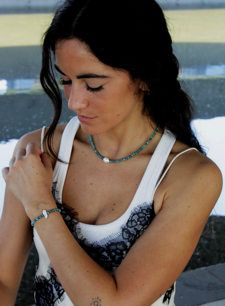 Woman wearing a white tank top with blue beaded pearl necklace and bracelet
