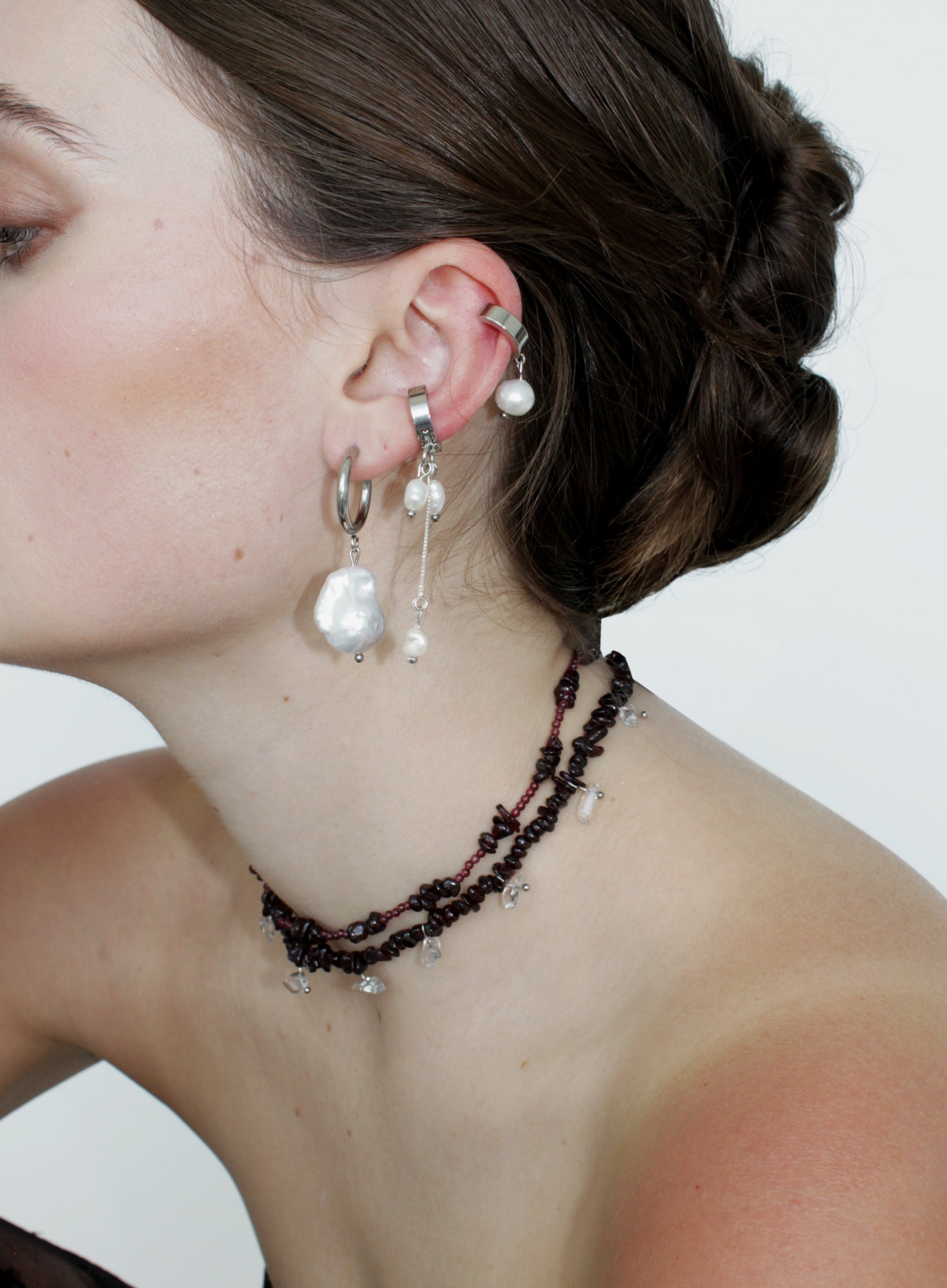 Close-up of a person wearing pearl earrings and red beaded necklaces against a white background