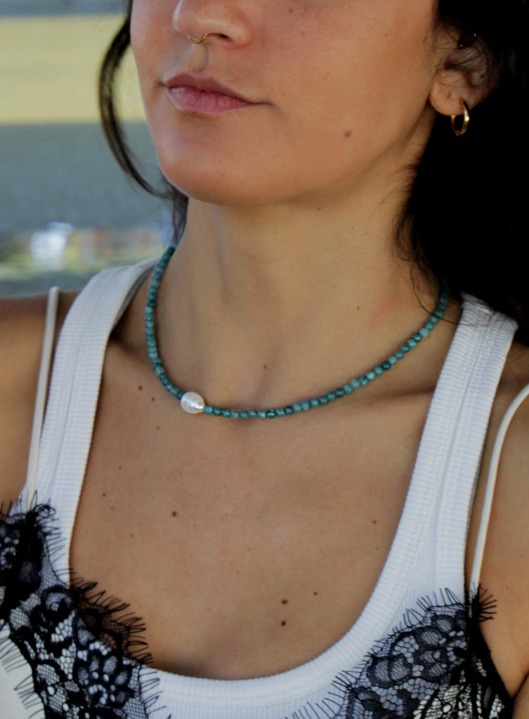 Woman wearing a white tank top with blue beaded pearl necklace