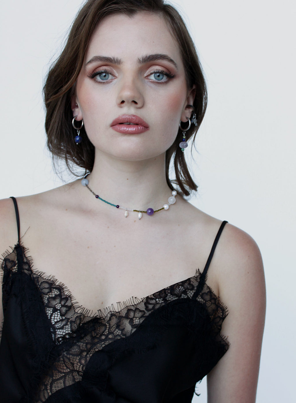 Woman wearing a black lace top and a beaded necklace against a white background