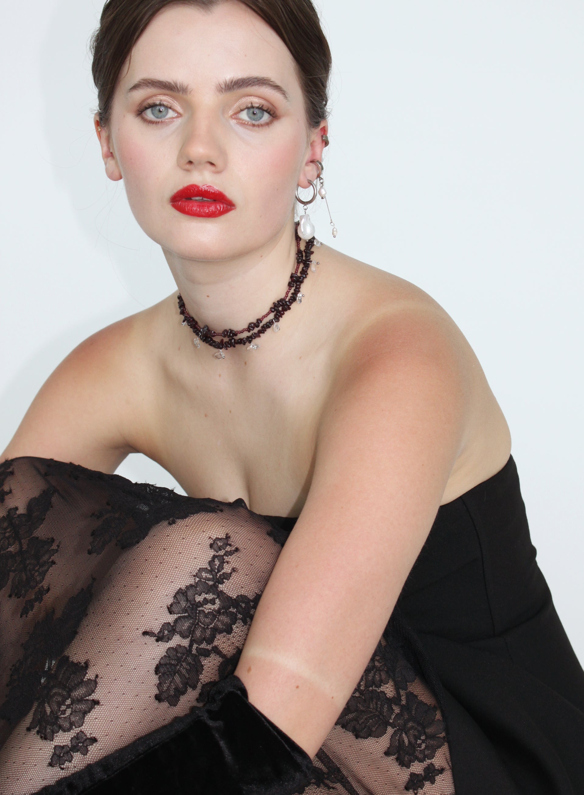 Woman wearing a black lace dress with red lipstick and red necklaces against a white background